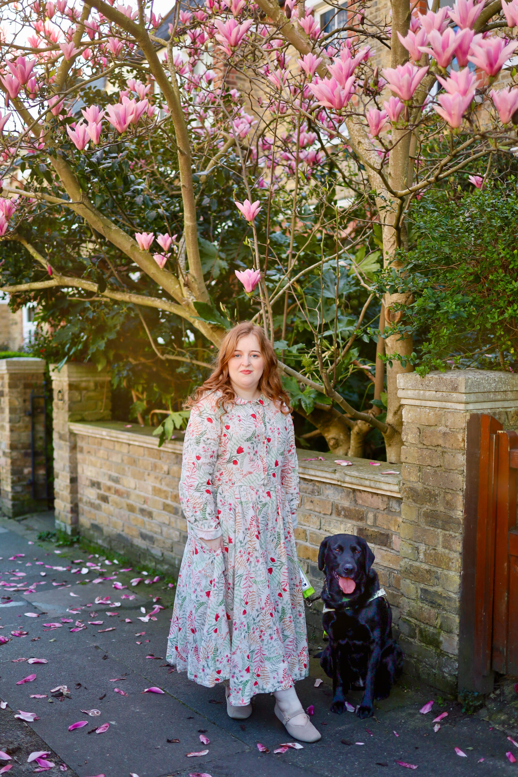Emily and guide dog Rosie standing in front of a magnolia blossom tree